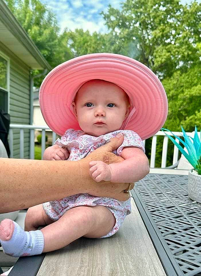 Gwen is registered to the contest to win money with this photo: baby, baby_toddler_clothing, cap, child, fashion_accessory, fun, grass, happy, hat, headwear, human_leg, leisure, person, pink, plant, recreation, sitting, sky, sun_hat, thigh