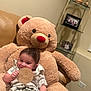 baby, teddy_bear, smile, infant, child, plush_toy, sign, wooden_sign, indoor, couch, sitting, clothing, shorts, shirt, photo_frame, shelf, home, cute, happy, portrait