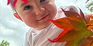 Emin is registered to the contest to win money with this photo: baby, child, face, smile, white_shirt, hand, autumn_leaves, red_leaves, orange_leaves, outdoor, nature, tree, foliage, sky, portrait, person, cute, happy, closeup, seasonal