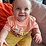 baby, child, smiling, happy, sitting, tshirt, shorts, orange, yellow, indoor, cushion, chair, person, cute, face, hands, eyes, expression, young, portrait