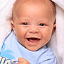 baby, infant, smile, happy, face, blue_shirt, blanket, flesh_tone, cute, child, newborn, young, human, portrait, closeup, skin, expression, joy, hand, warm