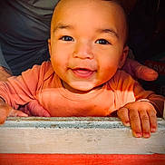 Mateo is registered to the contest to win money with this photo: baby, child, smile, happy, face, hands, orange_clothing, wooden_ledge, sunlight, portrait, closeup, infant, cute, warm_colors, indoor, person, young_child, expression, skin, eyes