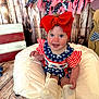 baby, child, smiling, red_bow, patriotic, american_flag, garland, wooden_background, cushion, white_socks, blue_eyes, cute, infant, sitting, clothing, decor, happy, portrait, indoor, celebration