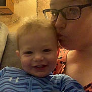 Ashton is registered to the contest to win money with this photo: adult, affection, blanket, blue, child, couch, deer, face, family, glasses, indoor, kiss, painting, person, portrait, smile, striped_clothing, toddler, wall, warm_lighting