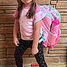 child, girl, portrait, standing, backpack, school, pink, bows, long_hair, brick_wall, wood_floor, sneakers, leggings, star_pattern, fashion, pouting, indoor, full_body, colorful, school_supplies