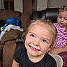 child, children, girl, smiling, portrait, indoor, living_room, couch, chair, black_shirt, pink_shirt, blonde_hair, braids, blue_eyes, happy, sitting, home, toy, family, watermark