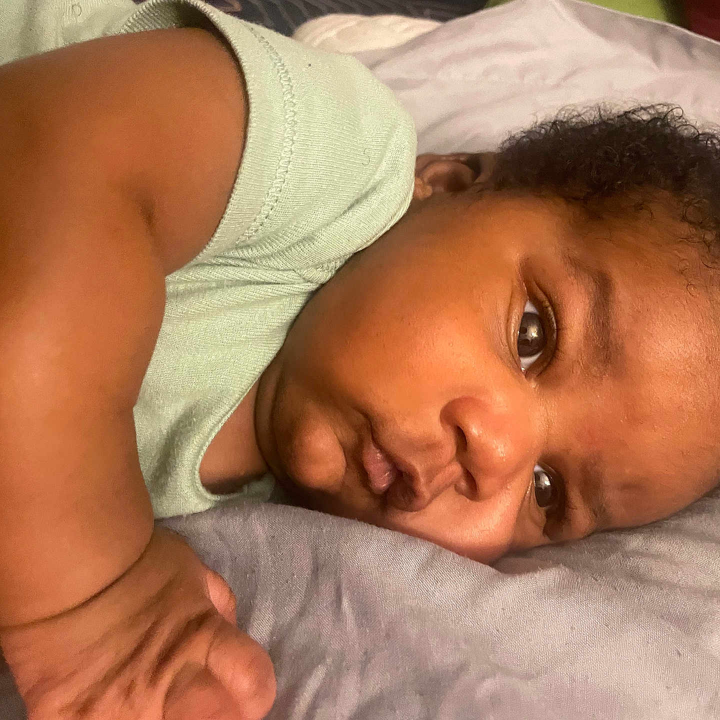 Adonis is registered to the contest to win money with this photo: arm, baby, bedding, cheek, closeup, curly_hair, cute, expression, eye, face, hand, indoors, infant, laying_down, nose, onesie, pillow, portrait, skin, sleepy