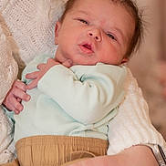 Kingston is registered to the contest to win money with this photo: baby, newborn, infant, portrait, close_up, holding, parent_hand, blanket, knit_sweater, mint_onesie, beige_pants, hand, face, eyes, mouth, hair, cozy, indoor, expression, watch