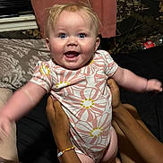 Indie is registered to the contest to win money with this photo: baby, infant, child, smiling, happy, blue_eyes, floral_onesie, arms_outstretched, hands_holding, indoor, bed, curtain, blanket, person, skin, joy, cute, young_child, human, portrait