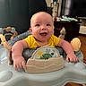 baby, smiling, indoor, yellow_shirt, activity_center, toys, happy, infant, furniture, television, wooden_floor, face, person, child, home, cute, plush_toy, seat, expression, bright