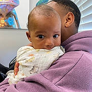 Lukas is registered to the contest to win money with this photo: baby, child, adult, hug, blanket, animal_print, purple_hoodie, indoor, window_blinds, painting, chameleon_art, face, eyes, curious, person, holding, portrait, closeup, skin, hand