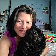 Peanut joined the competition — help win amazing prizes! bed, bedroom, black_dog, blanket, casual, cuddling, curly_hair, dog, face, furniture, happy, home_decor, indoor, person, pillow, portrait, smile, text_on_wall, wall_art, woman