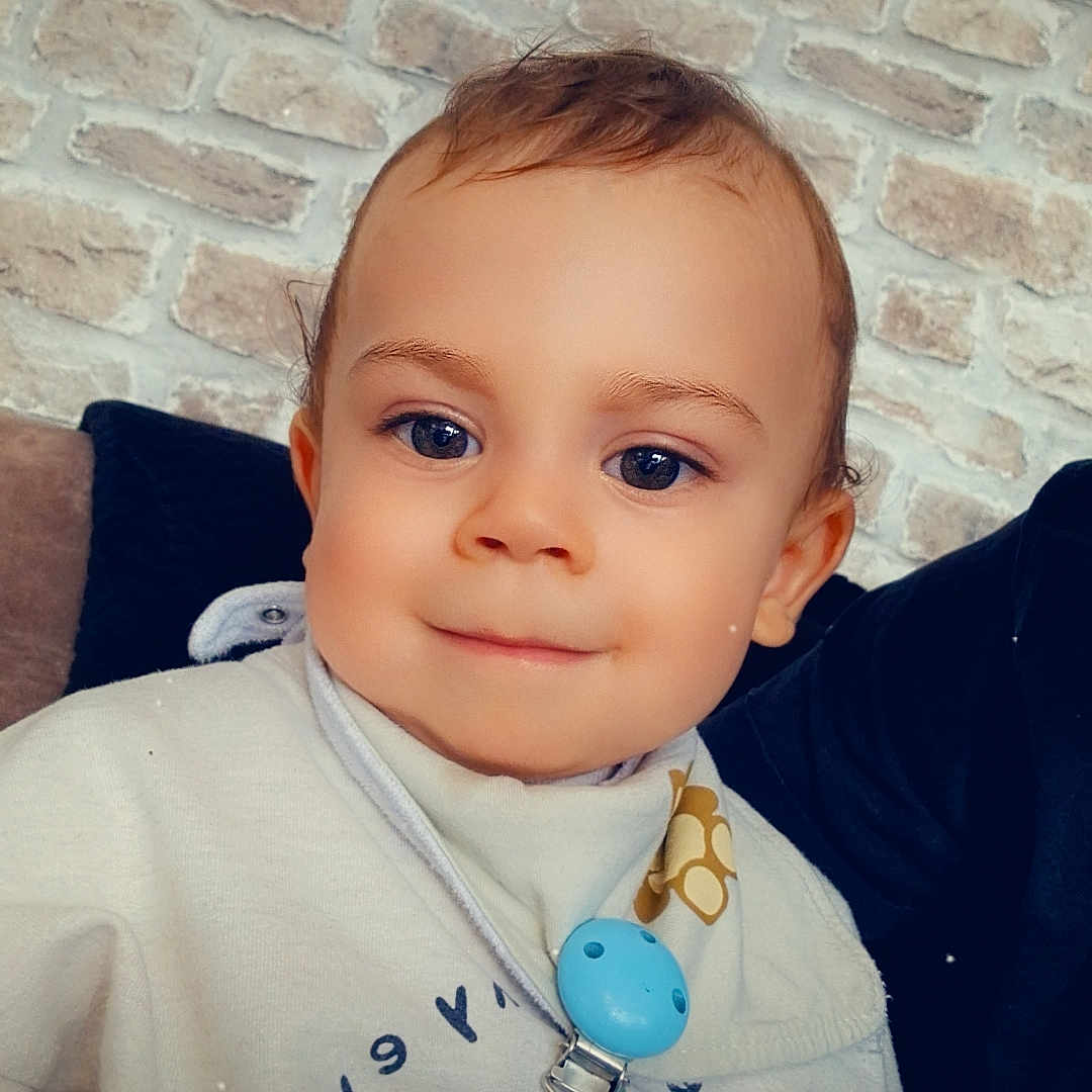 Raphaël a rejoint le concours — aidez-le/la à gagner de superbes lots ! accessory, baby, blue_eyes, brick_wall, casual, child, clothing, cozy, cute, face, happy, heart_emoji, indoor, pacifier, person, portrait, sitting, smile, toddler, young_child