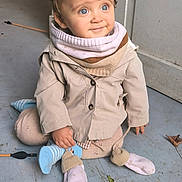 Alix a rejoint le concours — aidez-le/la à gagner de superbes lots ! toddler, child, blue_eyes, curly_hair, scarf, beige_jacket, socks, floor, bicycle, indoor, concrete, wall, sitting, smile, cute, curious, clothing, person, portrait, baby
