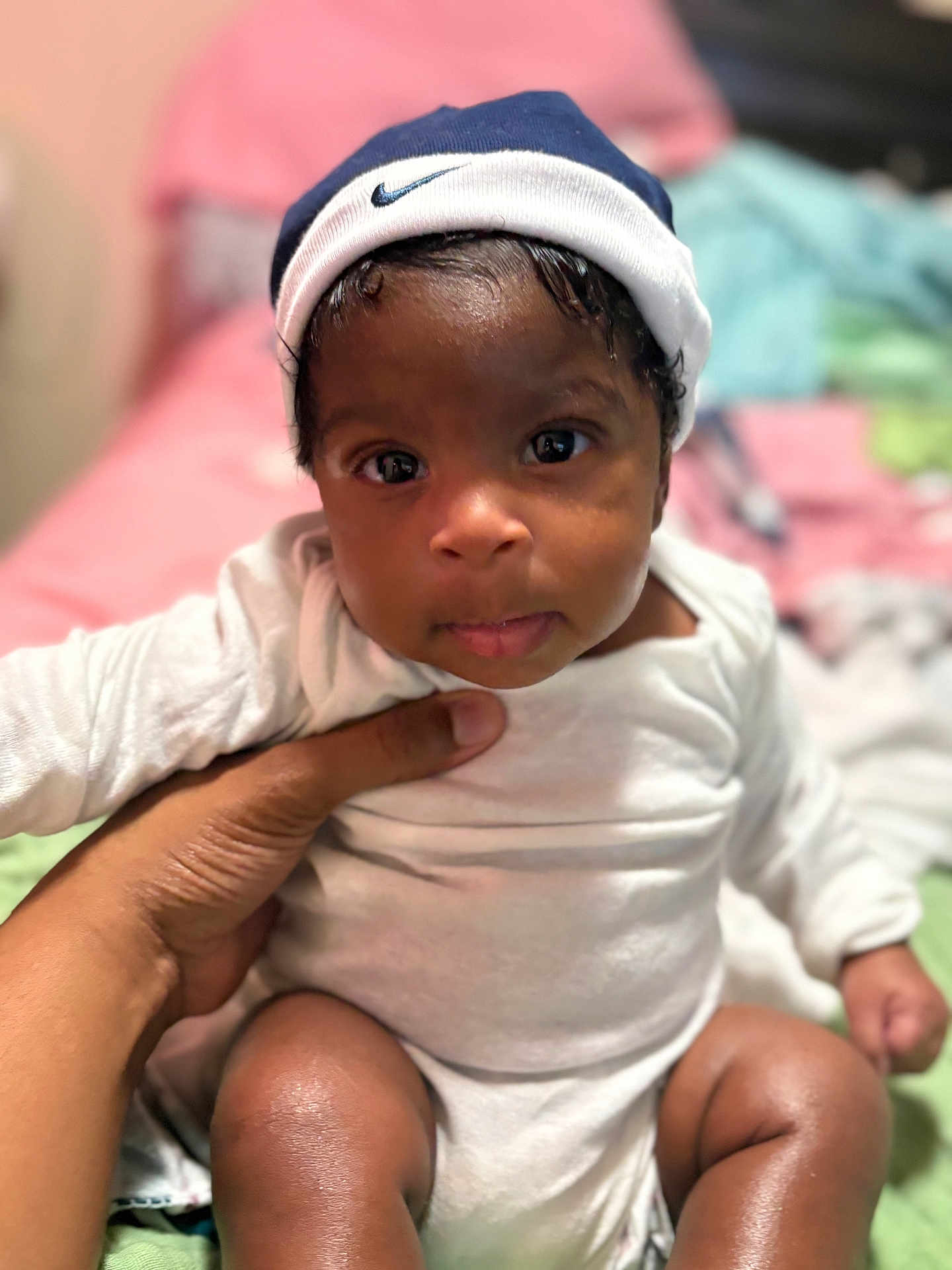 Aiden is registered to the contest to win money with this photo: baby, child, infant, person, face, hand, clothing, cap, nike, onesie, indoor, bed, blanket, skin, cute, portrait, sitting, expression, young, soft