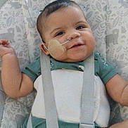 Gracen is registered to the contest to win money with this photo: adhesive_bandage, baby, baby_seat, child, close_up, face, feeding_tube, green_clothing, happy, harness, indoor, infant, medical_care, medical_tube, patterned_background, photography, portrait, seated, smiling, straps
