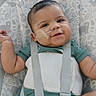 adhesive_bandage, baby, baby_seat, child, close_up, face, feeding_tube, green_clothing, happy, harness, indoor, infant, medical_care, medical_tube, patterned_background, photography, portrait, seated, smiling, straps
