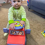 Nathan is registered to the contest to win money with this photo: baby, child, toy_car, pajamas, carpet, indoor, playtime, couch, cartoon, hands, feet, room, door, floor, toy, steering_wheel, cute, smiling, person, car