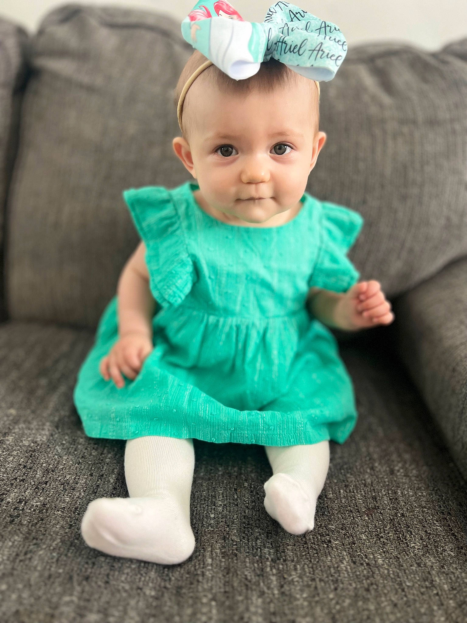 Charleigh is registered to the contest to win money with this photo: aqua, baby, baby_toddler_clothing, cap, cheek, child, clothing, costume_hat, couch, dress, fashion_accessory, grass, happy, hat, pattern, person, sitting, skin, sleeve, smile