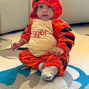 Avyansh is registered to the contest to win money with this photo: baby, child, tiger_costume, costume, orange, black, sitting, indoor, rug, carpet, portrait, face, eyes, hands, infant, cute, playful, home, furniture, textile