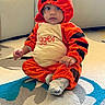 baby, child, tiger_costume, costume, orange, black, sitting, indoor, rug, carpet, portrait, face, eyes, hands, infant, cute, playful, home, furniture, textile