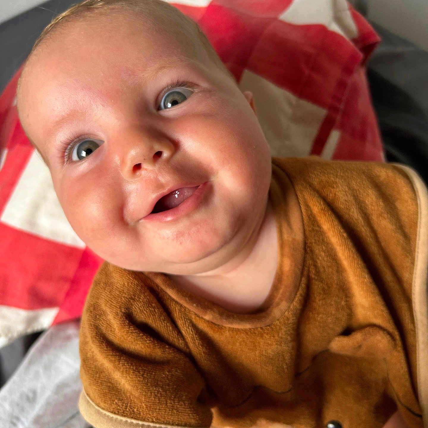 Jules participe au concours pour gagner de l'argent avec cette photo : baby, bed, blanket, blue_eyes, brown_clothing, child, close_up, cute, expression, face, happy, indoor, infant, joyful, person, portrait, red_and_white, skin, smiling, young_child