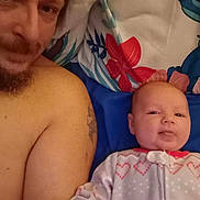 Margaret Hamilton is registered to the contest to win money with this photo: baby, beard, bed, blanket, candid, face, family, floral_pattern, heart_pattern, indoors, infant, man, onesie, person, portrait, relaxing, shirtless, skin, tattoo, tongue_out