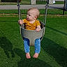 baby, child, swing, playground, outdoor, grass, fence, park, daylight, curious, infant, casual_clothing, barefoot, greenery, trees, sunlight, seat, play, baby_clothes, blue_pants