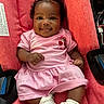 baby, infant, smile, pink_clothing, red_seat, cushion, cute, child, happy, person, portrait, sitting, indoors, sock, curly_hair, face, skin, hand, footwear, car_seat