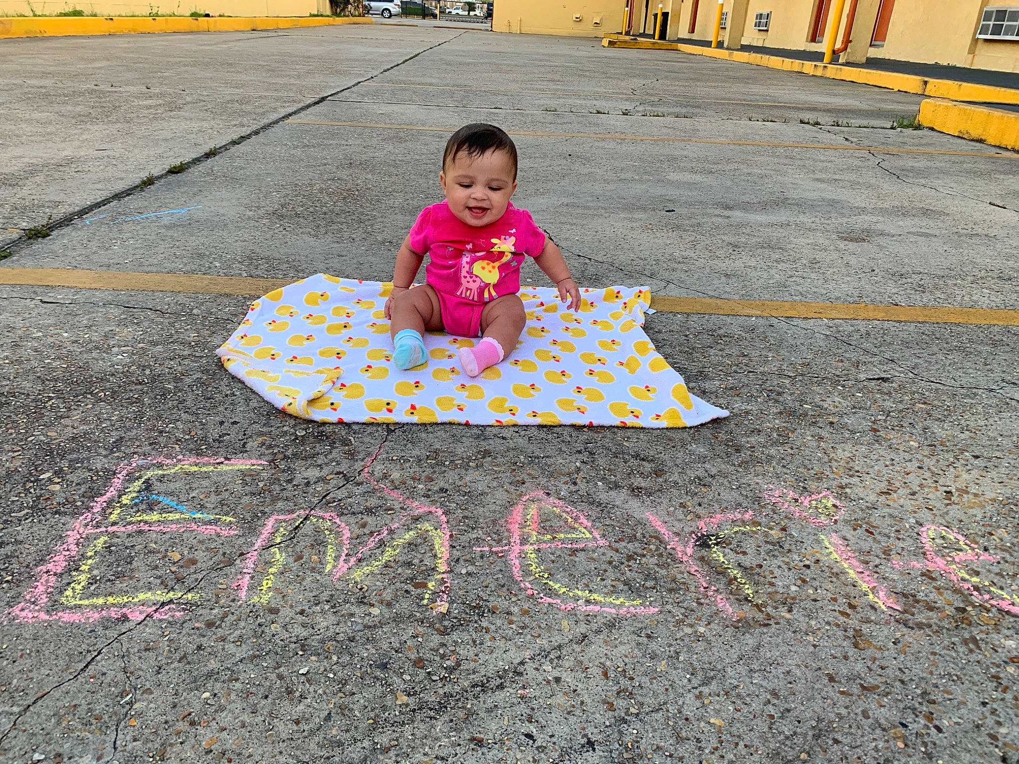 Emerie is registered to the contest to win money with this photo: asphalt, chalk, child, city, concrete, event, flooring, font, fun, handwriting, person, poster, public_space, road, road_surface, sidewalk, tar, tire, toddler, wheel