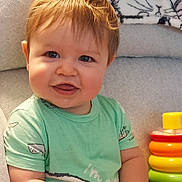 Grayson joined the competition — help win amazing prizes! baby, child, smiling, green_shirt, toy, stacking_toy, couch, blanket, bunny_pattern, indoor, cute, happy, portrait, toddler, playful, cheerful, person, young_child, sitting, infant