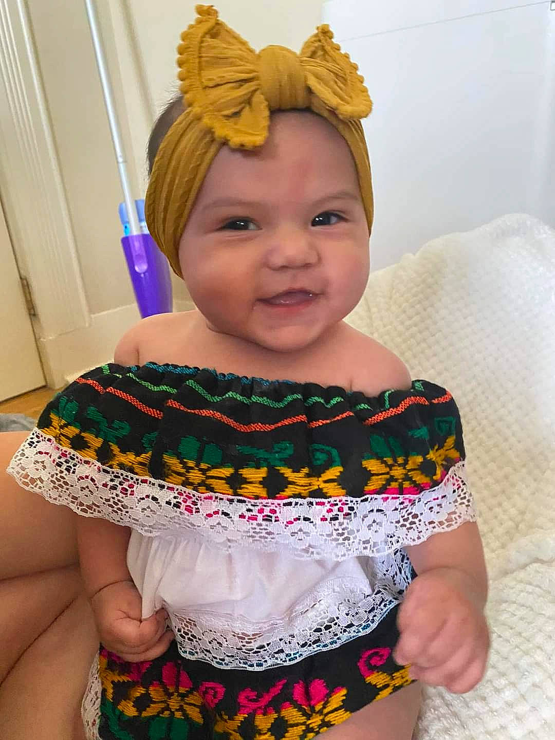 Gisele is registered to the contest to win money with this photo: baby_toddler_clothing, embellishment, fashion, fashion_design, happy, headpiece, headwear, human_body, iris, jewellery, neck, organ, pattern, person, pink, product, skin, sleeve, smile, textile