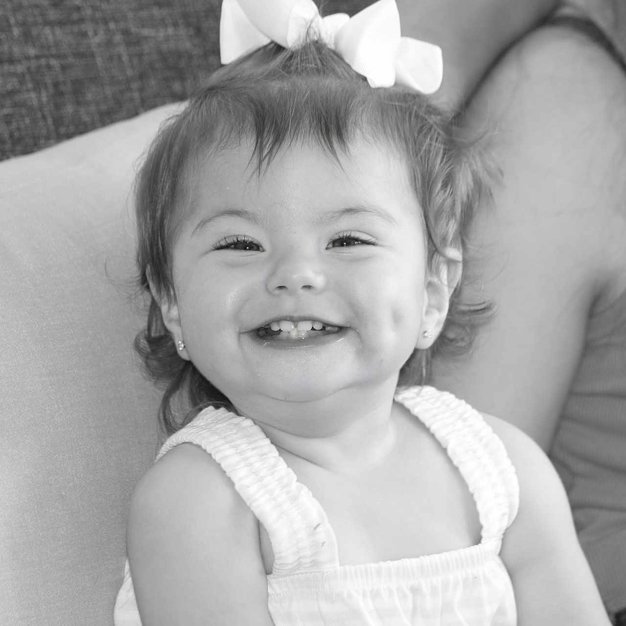 Madelyn joined the competition — help win amazing prizes! baby, black_and_white, bow, child, clothing, couch, cute, dimples, earrings, face, family, hair, happy, indoor, joy, person, portrait, sitting, smile, toddler