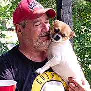 Daisy Mae joined the competition — help win amazing prizes! man, dog, red_cap, outdoor, greenery, black_tshirt, guns_n_roses, pet, holding, beard, cup, small_dog, white_dog, brown_dog_face, affection, portrait, nature, daylight, casual, happy