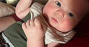 Malakai is registered to the contest to win money with this photo: baby, infant, child, face, blue_eyes, bib, clothing, couch, indoor, person, skin, cheeks, hand, fist, portrait, cozy, warm_lighting, expression, cute, home