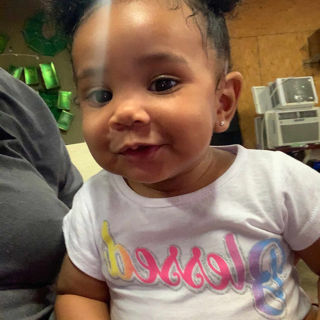 Minyah joined the competition — help win amazing prizes! baby, background, child, cozy, curly_hair, cute, earrings, face, fringed_shirt, furniture, hand, indoor, light, person, portrait, puffs, smiling, toddler, white_shirt, yellow_shorts