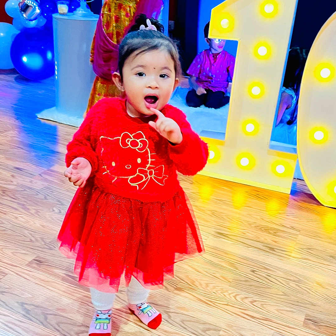 Aratrika joined the competition — help win amazing prizes! balloons, birthday, celebration, child, cute, decorations, event, floor, hello_kitty, indoor, lighting, number_one, party, people, person, red_dress, smiling, socks, toddler, wooden_floor
