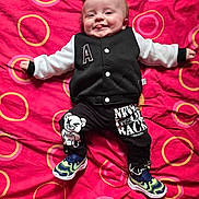 Mayronn a rejoint le concours — aidez-le/la à gagner de superbes lots ! baby, child, smiling, tongue_out, blanket, red, circles, clothing, jacket, pants, sneakers, cute, happy, lying_down, pattern, graphic_design, infant, person, indoors, playful