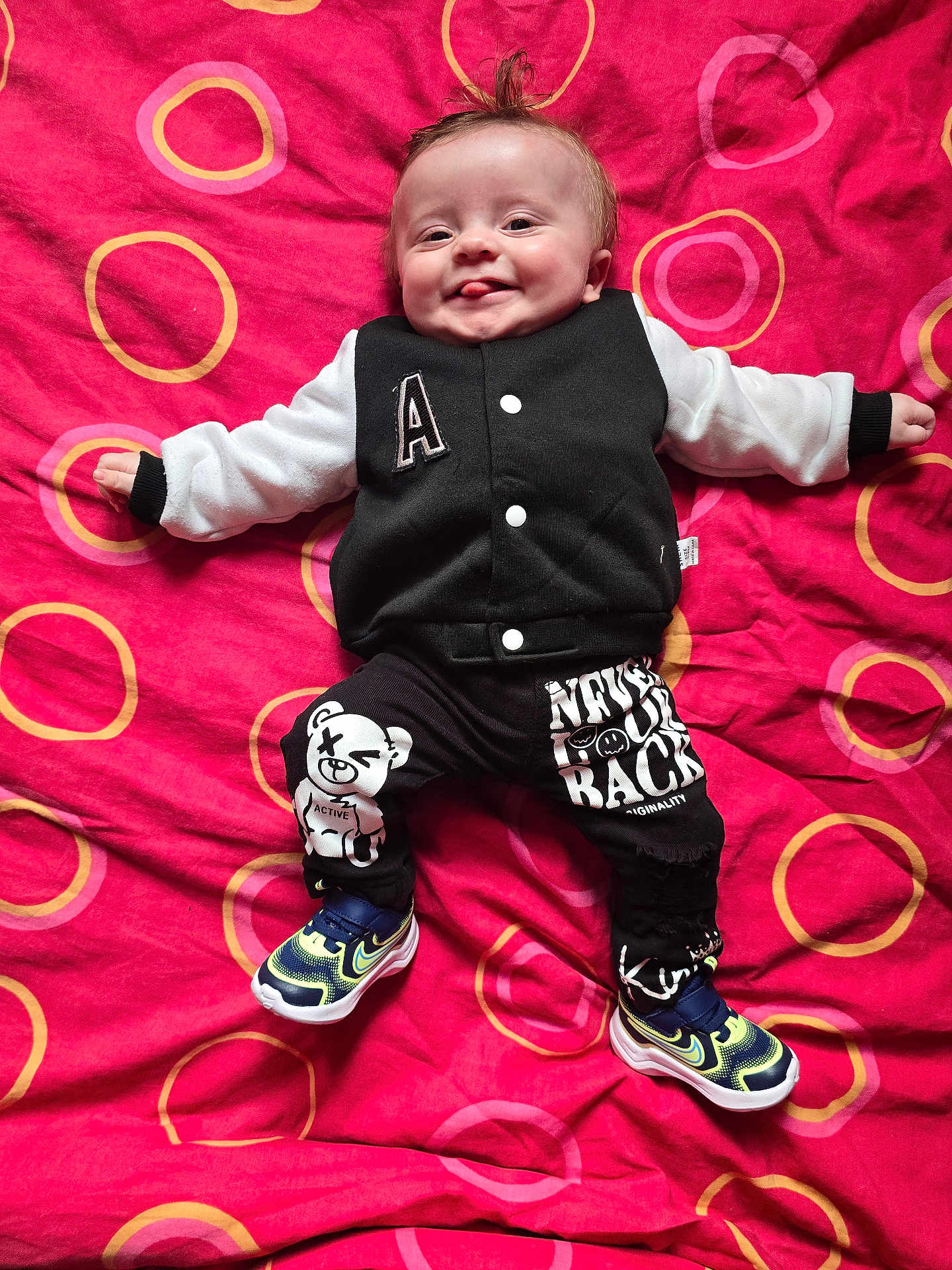 Mayronn a rejoint le concours — aidez-le/la à gagner de superbes lots ! baby, child, smiling, tongue_out, blanket, red, circles, clothing, jacket, pants, sneakers, cute, happy, lying_down, pattern, graphic_design, infant, person, indoors, playful