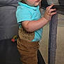 baby, blue_shirt, brown_pants, cartoon, child, curious, face, foot, holding, indoor, infant, living_room, mesh, nine_months, playpen, portrait, skin, standing, television, wooden_sign