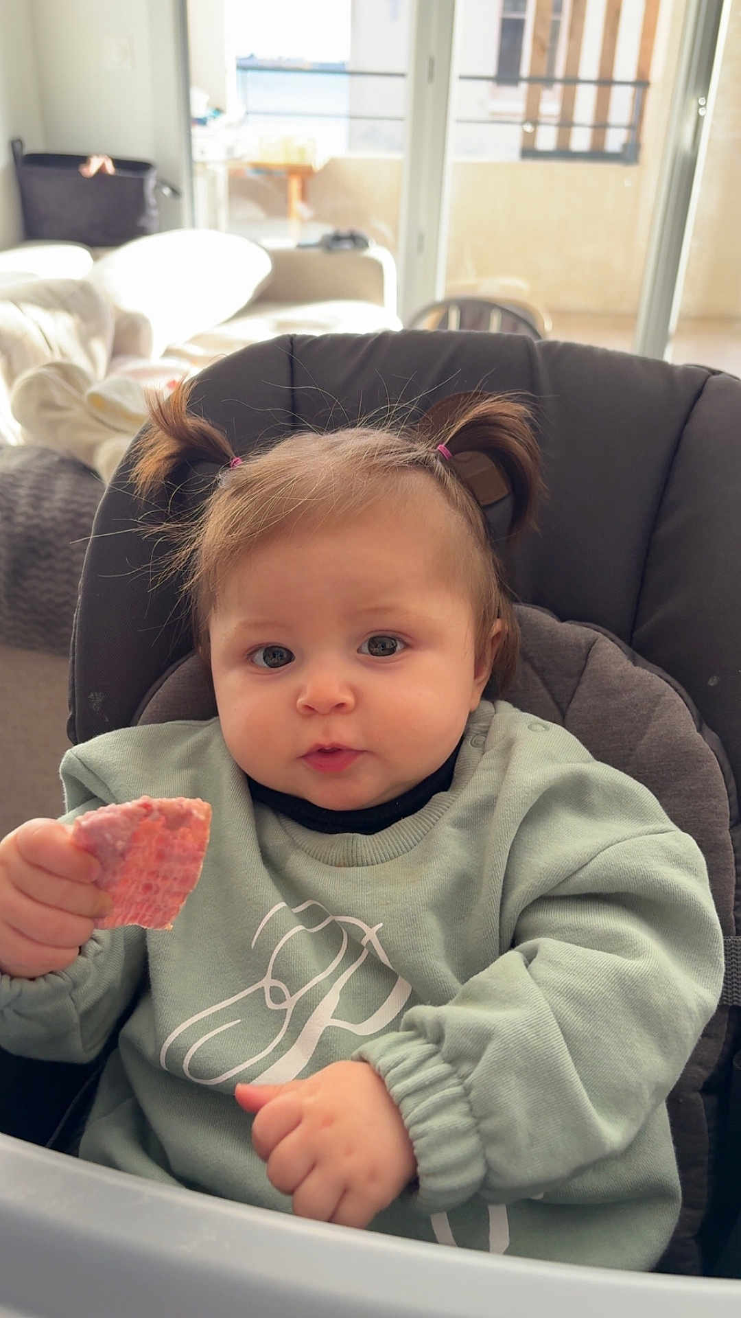 Giulia a rejoint le concours — aidez-le/la à gagner de superbes lots ! baby, child, pigtails, high_chair, cookie, food, indoor, sweatshirt, person, cute, face, hand, table, window, natural_light, cozy, expression, young_child, sitting, curious