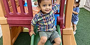 Damian Politz is registered to the contest to win money with this photo: child, toddler, playground, slide, smiling, plaid_shirt, shorts, sneakers, outdoor, play_equipment, green_slide, artificial_grass, happy, cute, fun, kids, recreation, young_child, daylight, playing