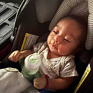 Issac is registered to the contest to win money with this photo: baby, car_seat, bottle, blanket, infant, child, clothing, seat_belt, soft_lighting, indoors, portrait, cute, young_child, person, resting, casual, warm, comfort, relaxed, toddler