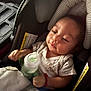 baby, car_seat, bottle, blanket, infant, child, clothing, seat_belt, soft_lighting, indoors, portrait, cute, young_child, person, resting, casual, warm, comfort, relaxed, toddler