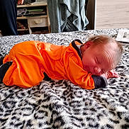 Ava a rejoint le concours — aidez-le/la à gagner de superbes lots ! baby, newborn, orange_outfit, blanket, bed, sleeping, smile, face, socks, patterned_blanket, bedroom, furniture, drawer, person_partial, hand, cozy, infant, portrait, soft_texture, lying_down