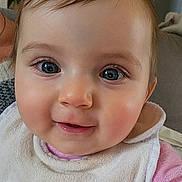 Ambre participe au concours pour gagner de l'argent avec cette photo : baby, infant, face, eyes, eyelashes, cheeks, smile, bib, drool, close_up, portrait, skin, hair, pink_clothing, couch, indoor, toddler, gaze, eye_reflection, adorable