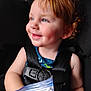child, toddler, smile, blue_eyes, red_hair, curly_hair, dimple, car_seat, seatbelt, safety_harness, ziplock_bag, hand, portrait, closeup, profile, cheek, skin, happy, vehicle_interior, clothing