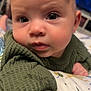 baby, infant, face, eyes, sweater, green_clothing, close_up, indoor, blanket, pattern, curious, skin, head, child, portrait, young, cute, expression, person, toddler