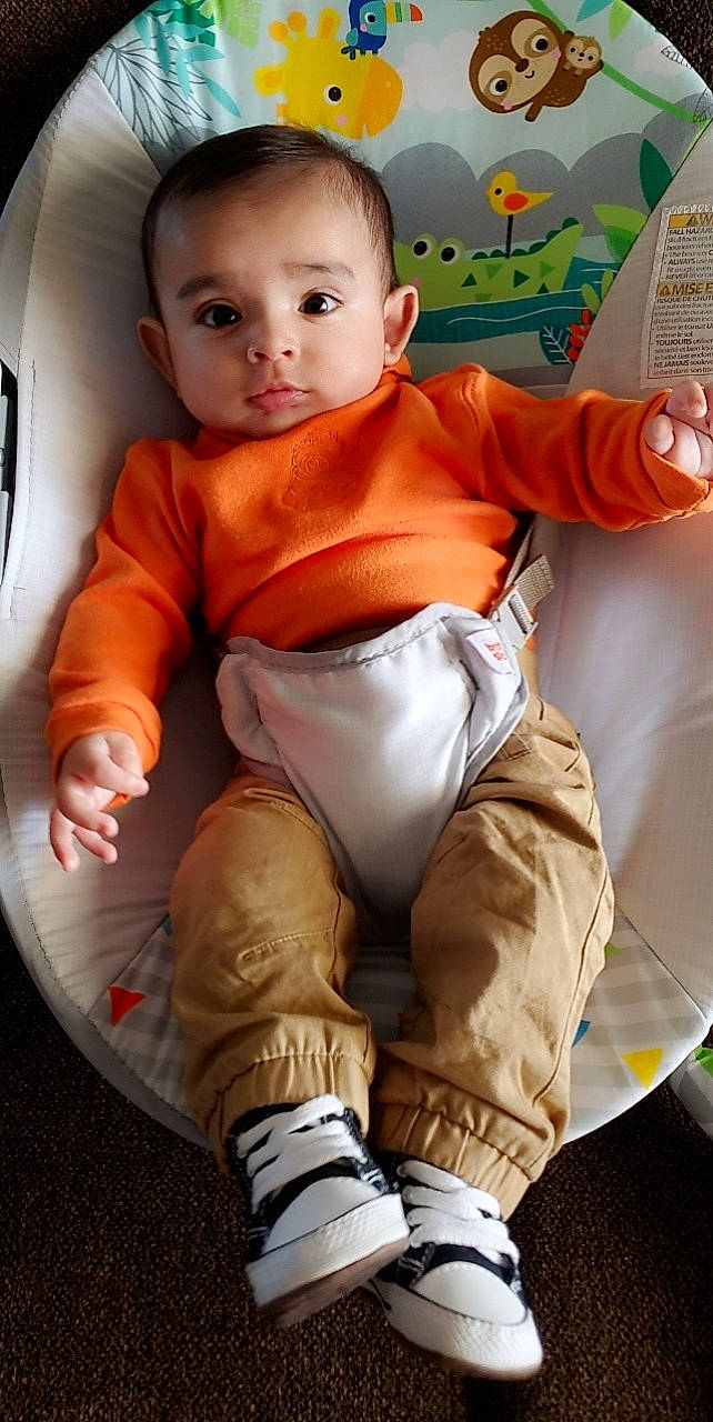 Elian is registered to the contest to win money with this photo: baby, baby_toddler_clothing, car_seat, chair, child, comfort, finger, fun, human_leg, joint, knee, orange, person, sitting, skin, sleeve, sock, thigh, thumb, toddler