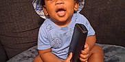 Tylan joined the competition — help win amazing prizes! toddler, child, baby, hat, bucket_hat, blue_clothing, socks, remote_control, couch, blanket, indoor, happy, smiling, seated, furniture, person, cute, curious, young_child, home